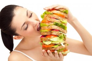 O femeie luand o gura dintr-un sandwich urias